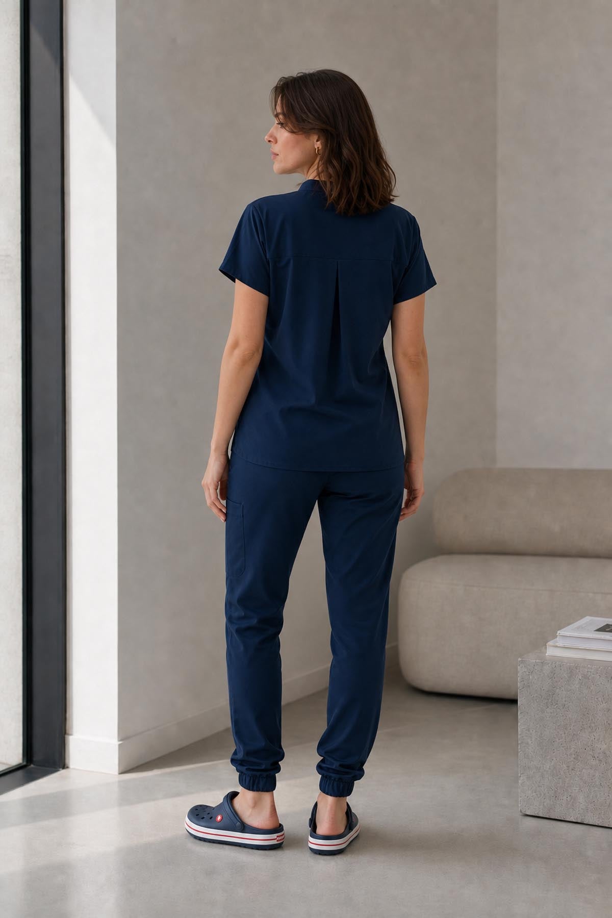 Asistenta medicala purtand bluza uniforma medicala bleumarin unisex, model Scrub Activity, vedere din spate