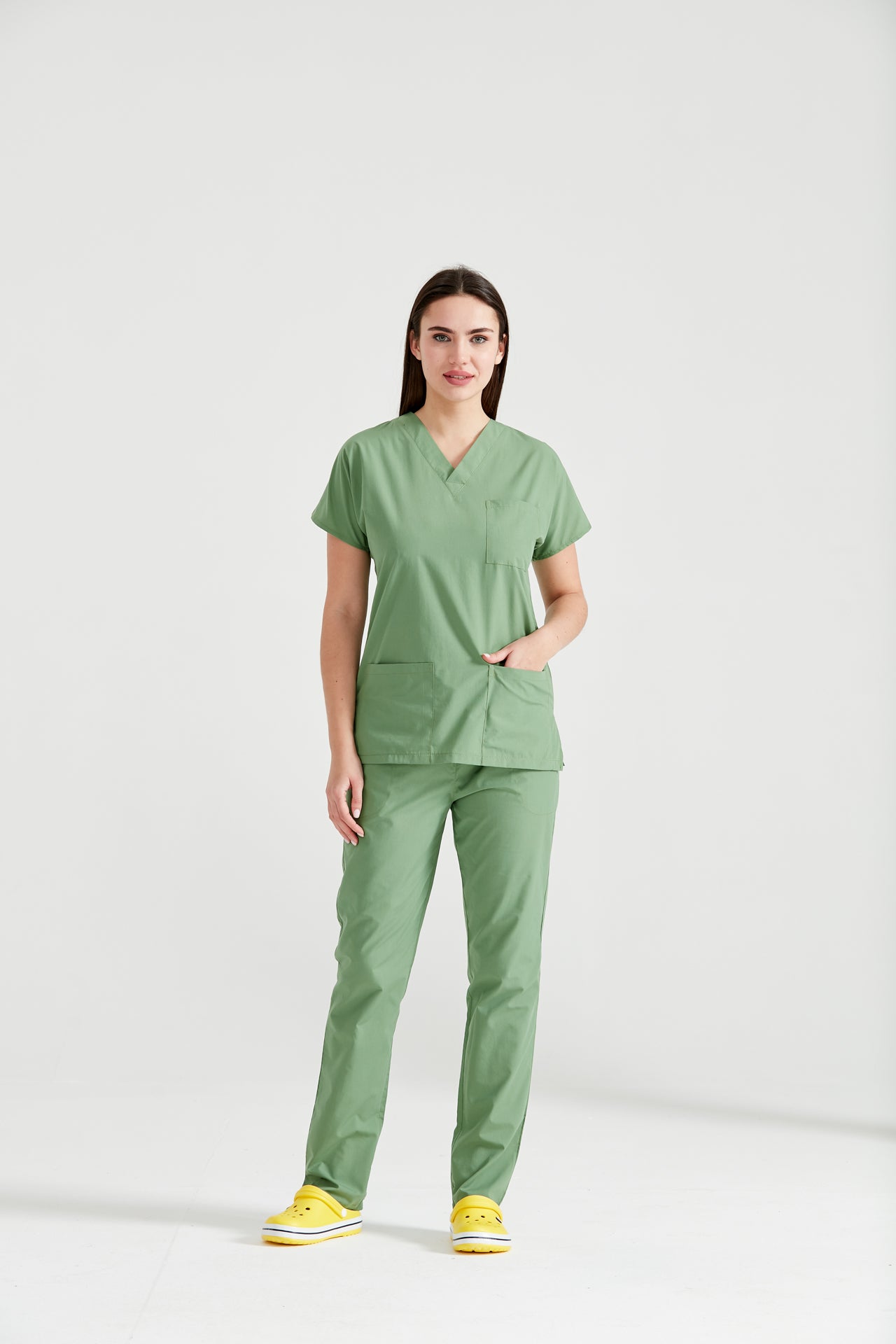 Asistenta medicala imbracata in costum medical verde fistic Pistaccio, cu mainile in buzunar, vedere din fata