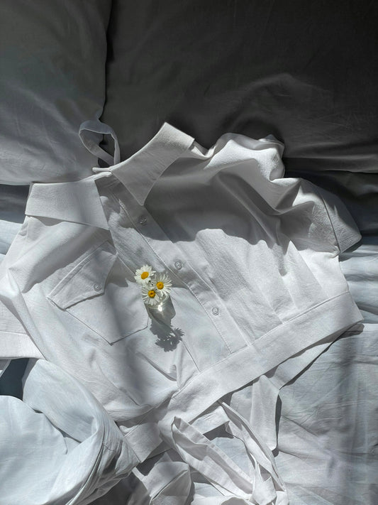 a white shirt laying on top of a bed next to a flower