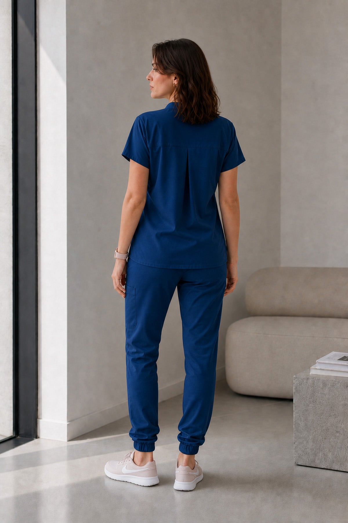 Asistenta medicala purtand bluza uniforma medicala albastru indigo unisex, model Scrub Activity, vedere din spate