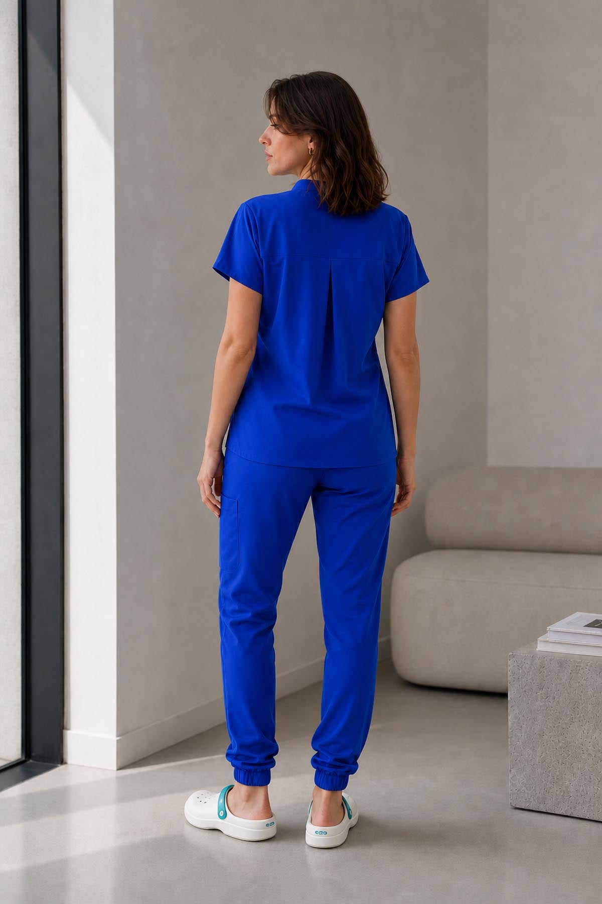 Asistenta medicala purtand bluza uniforma medicala albastru regal unisex, model Scrub Activity, vedere din spate