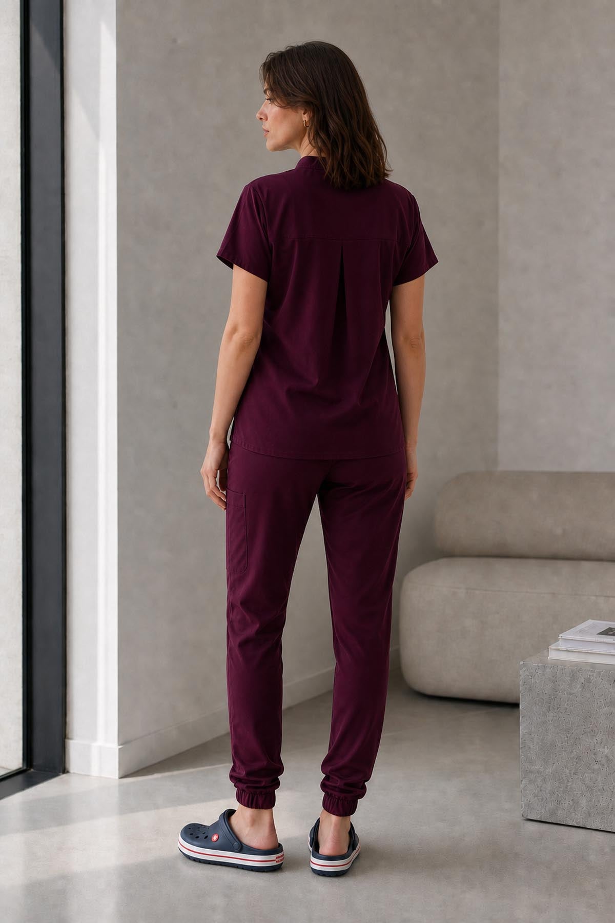 Asistenta medicala purtand bluza uniforma medicala grena unisex, model Scrub Activity, vedere din spate