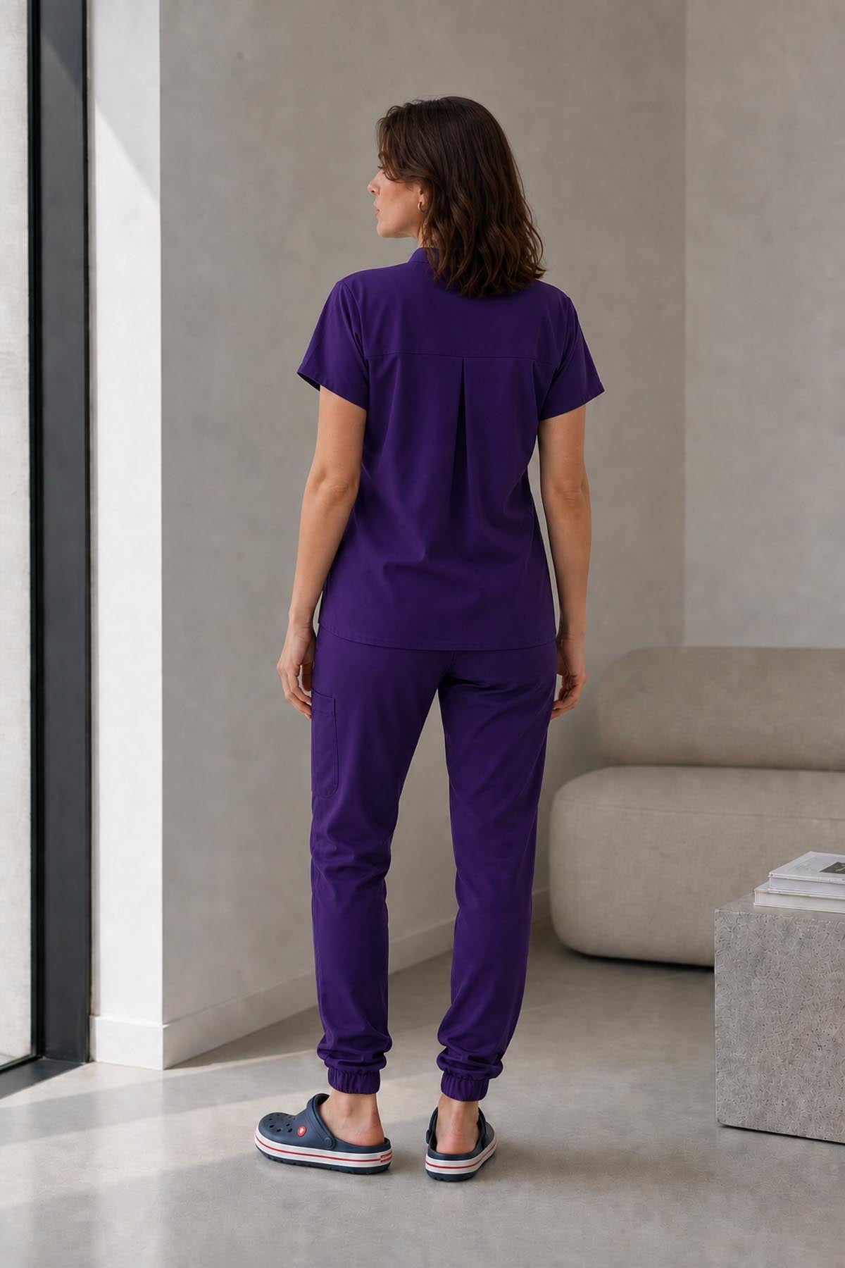 Asistenta medicala purtand bluza uniforma medicala mov unisex, model Scrub Activity, vedere din spate