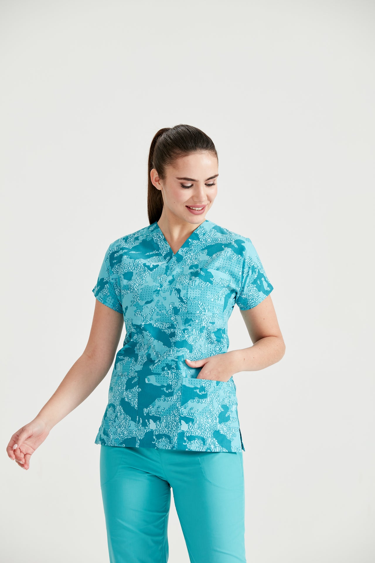 Asistenta medicala imbracata in bluza Camouflage Turquoise, cu mana in buzunar, vedere din fata