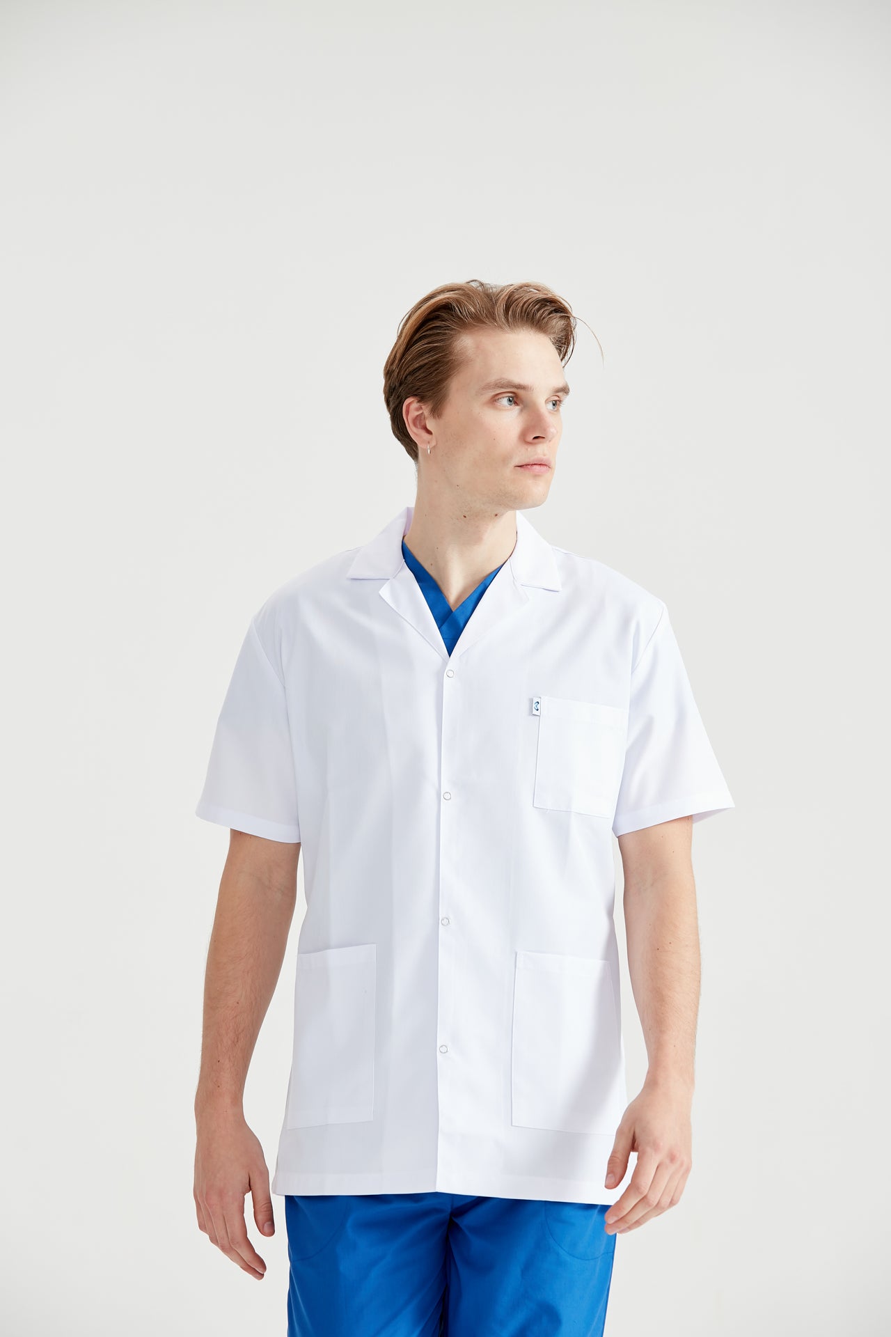 Asistent medical imbracat in halat Dr. Rever Summer, cu mainile in buzunar, vedere din semiprofil