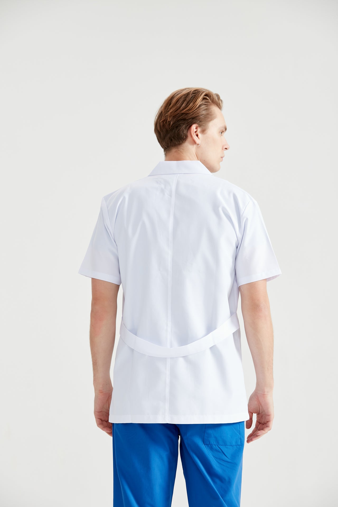 Asistent medical imbracat in halat Dr. Rever Summer, cu mainile in buzunar, vedere din spate