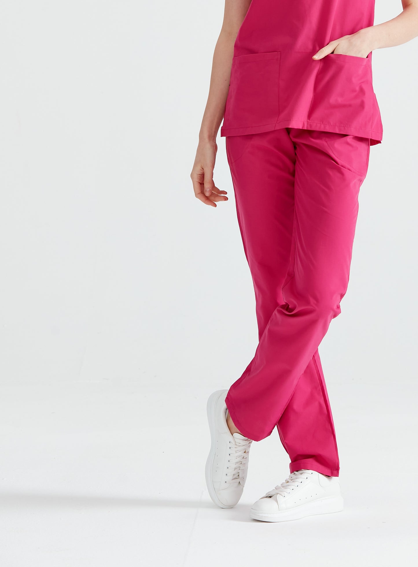 Asistenta medicala imbracata in pantaloni Fuchsia, cu picioarele incrucisate, vedere din fata