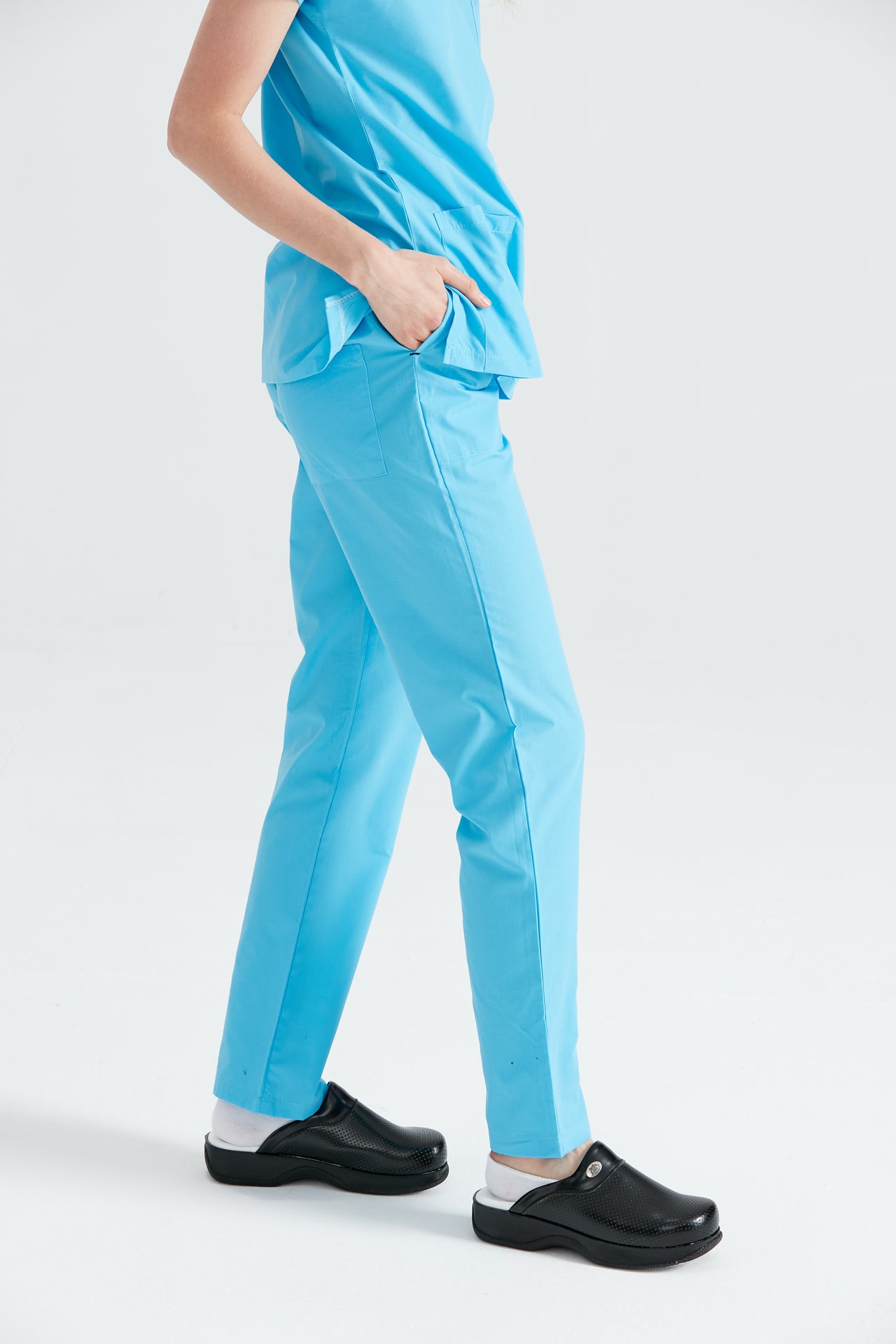 Asistenta medicala imbracata in pantaloni Turquoise, cu mana in buzunar, vedere din profil